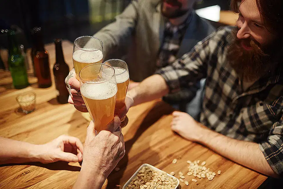 A group of friends responsibly toasting beer glasses at a bar after completing online training on responsible beverage service.